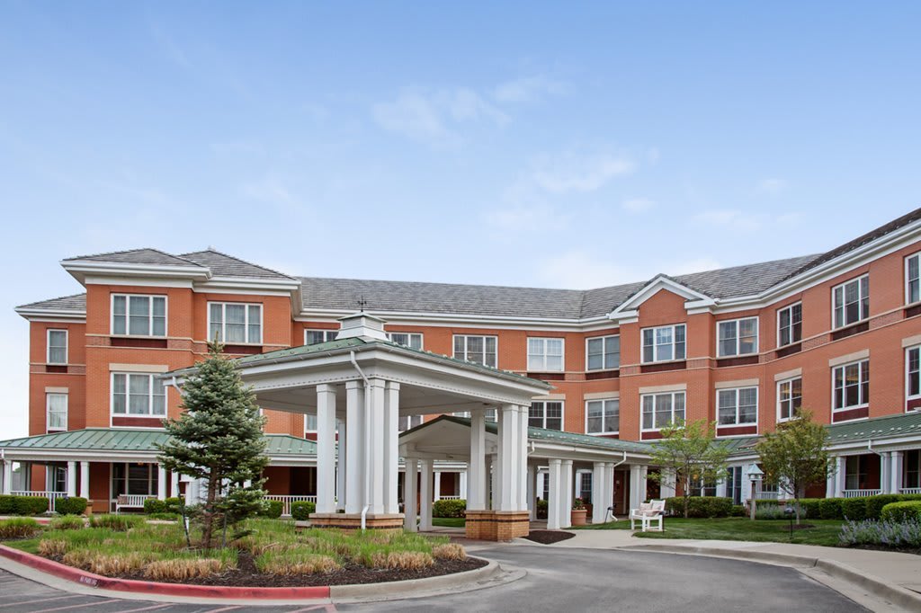 A modern multi-story brick building with a grand entrance and landscaped surroundings.
