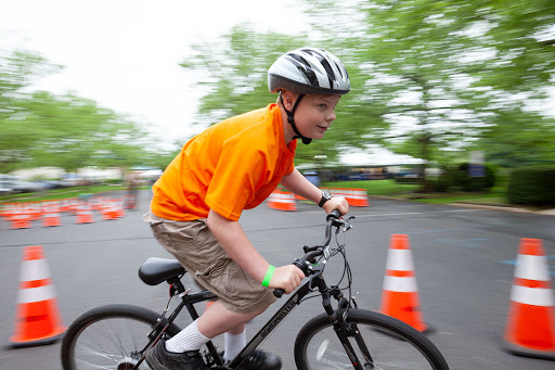 A child riding a bicycle wearing a helmet, navigating through cones in an outdoor setting.