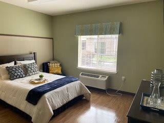 A cozy, minimalist bedroom featuring a single bed with white and blue bedding, a wooden floor, and green-painted walls.