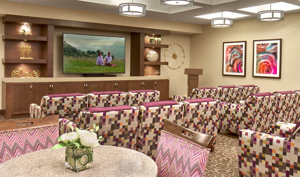 A modern conference room with patterned chairs, a large screen, and diverse artwork.