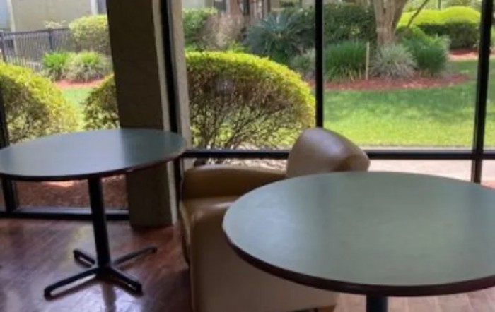 A cozy seating area with round tables and chairs next to a large window overlooking a garden.
