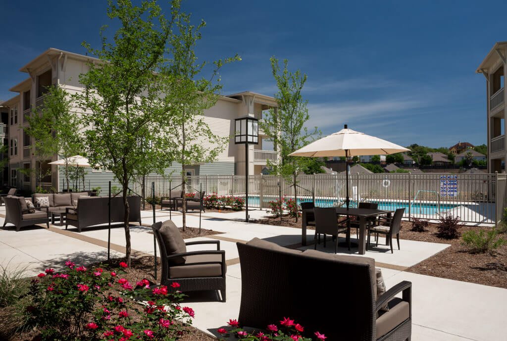 A relaxing poolside patio area with seating and umbrellas, surrounded by landscaped greenery and flowers.