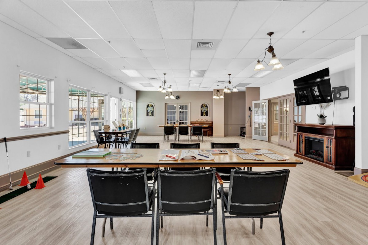 A spacious meeting room setup with tables and chairs, featuring ceiling fans and large windows.