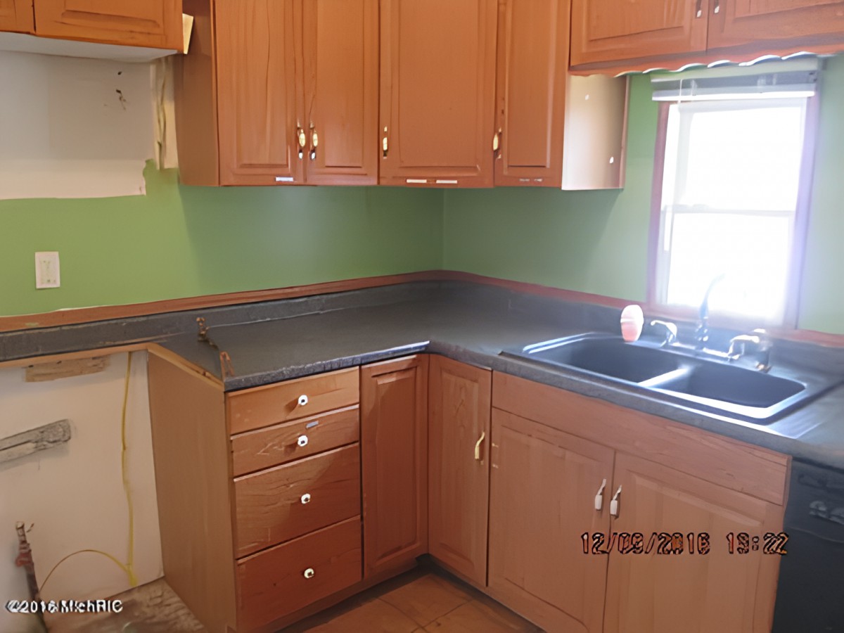 A kitchen with wooden cabinets, a dark countertop, and a green painted wall.