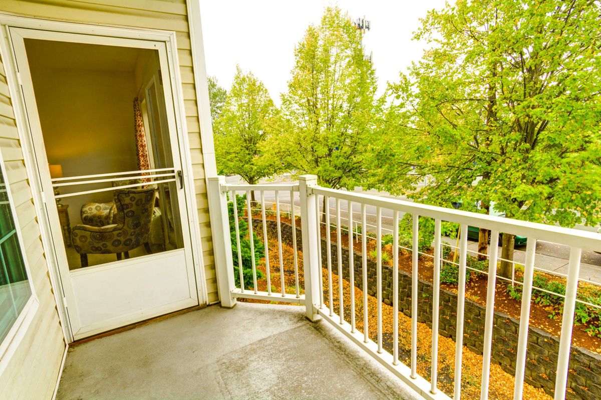 A small residential balcony with a white railing overlooks lush green trees.