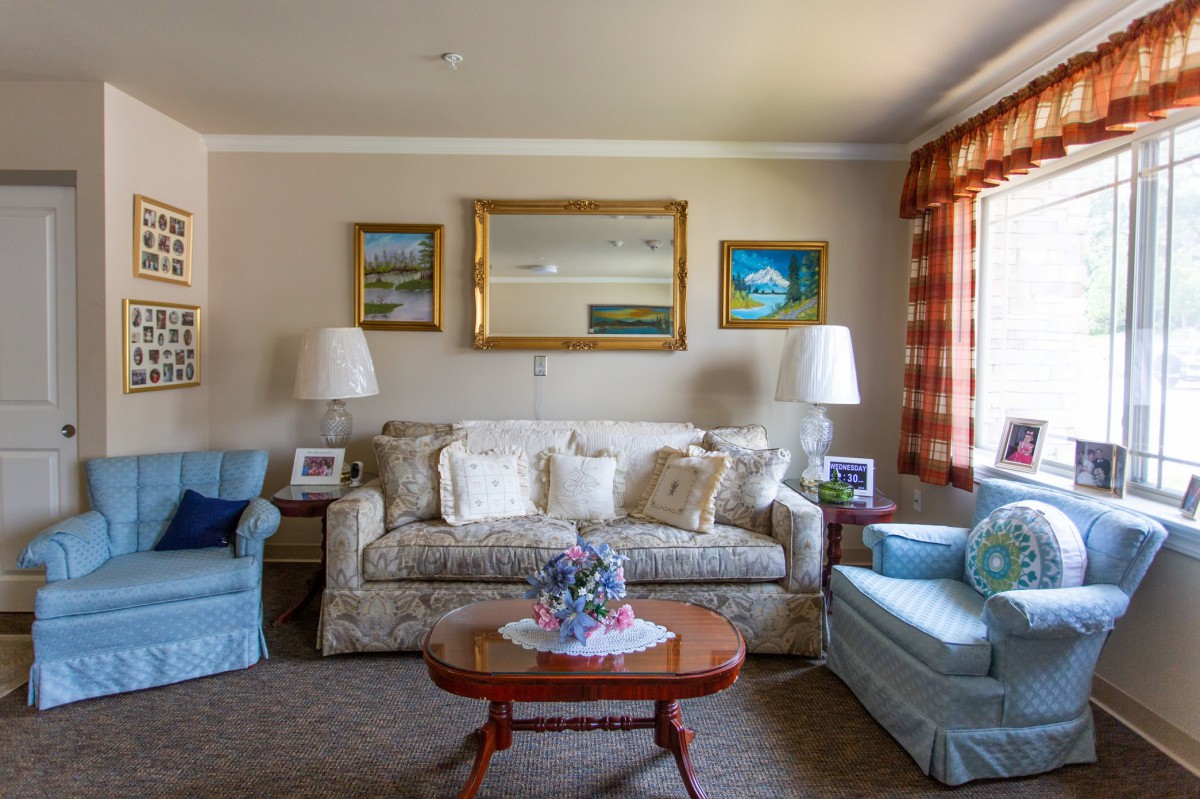 A cozy living room with a sofa, armchairs, and a coffee table, elegantly decorated with paintings and lamps.