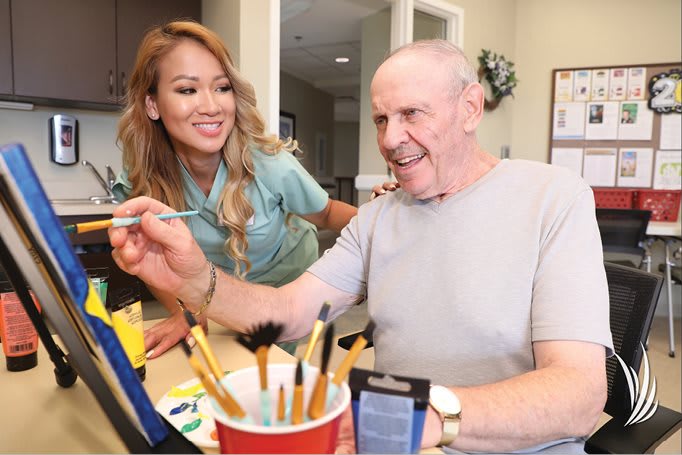 A nurse assists an elderly man during a painting session.
