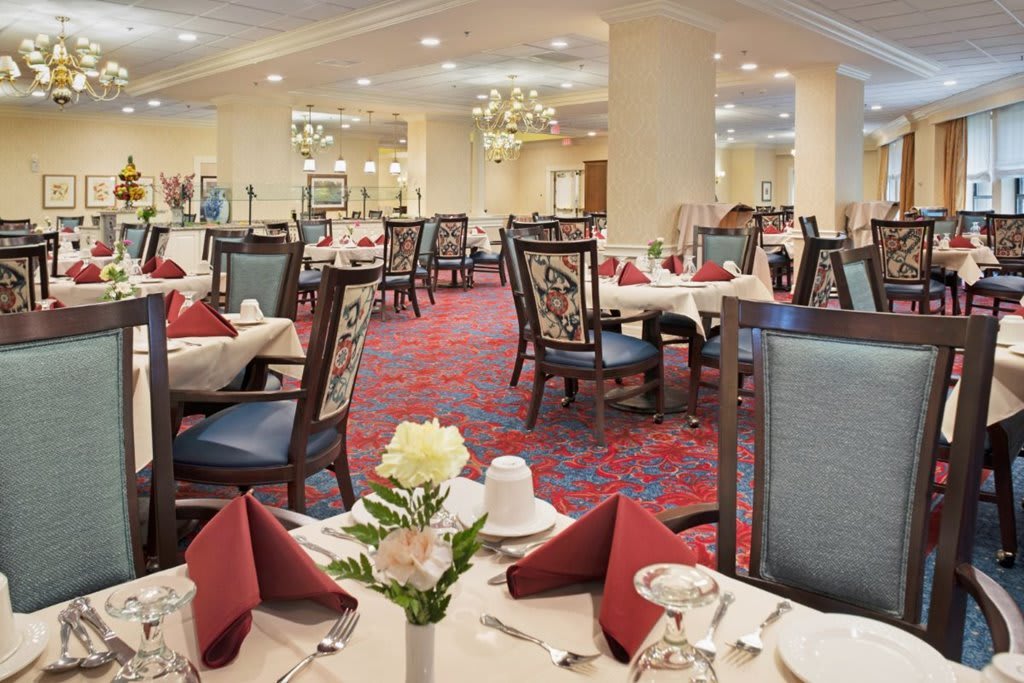 A spacious, elegantly decorated dining area with neatly arranged tables and chairs, featuring chandeliers and floral centerpieces.