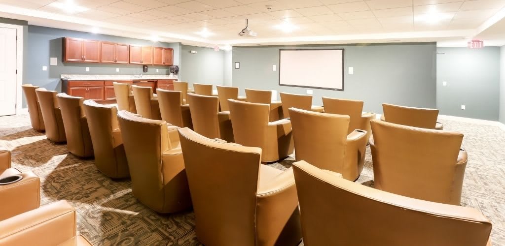 A small theater-style conference room with leather chairs facing a screen.