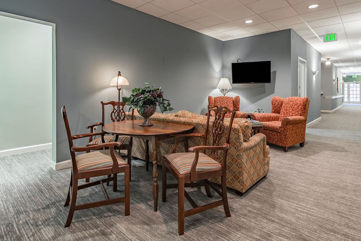A cozy living room with a round wooden table, cushioned chairs, and a wall-mounted TV.