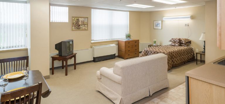 A cozy living room with a sofa, television, and dresser near a window.