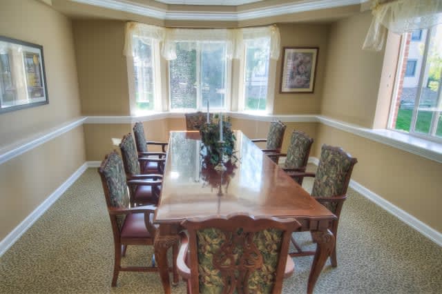 A well-lit dining room with a large wooden table and upholstered chairs.