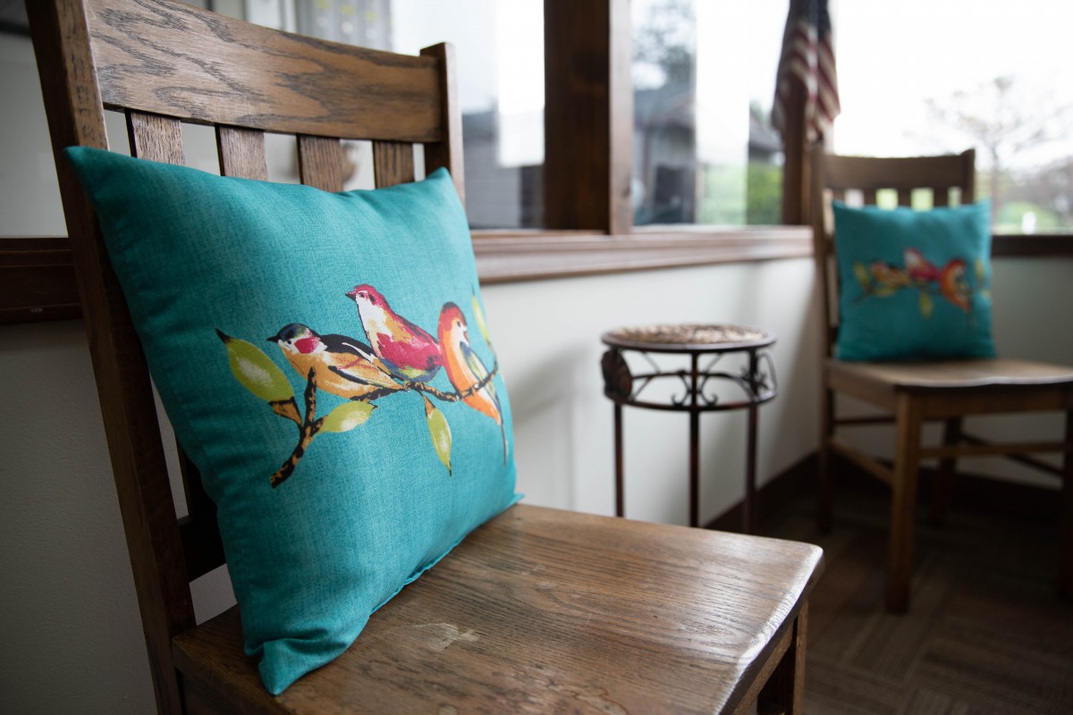 A cozy porch featuring a wooden rocking chair adorned with a colorful bird-themed pillow.