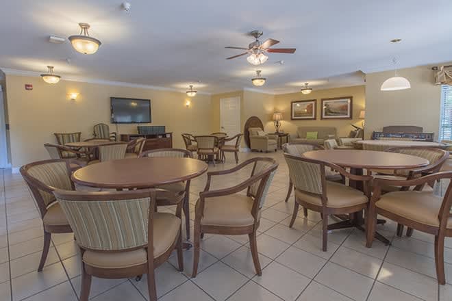 A spacious dining area with multiple tables and chairs, featuring ceiling fans and soft lighting.