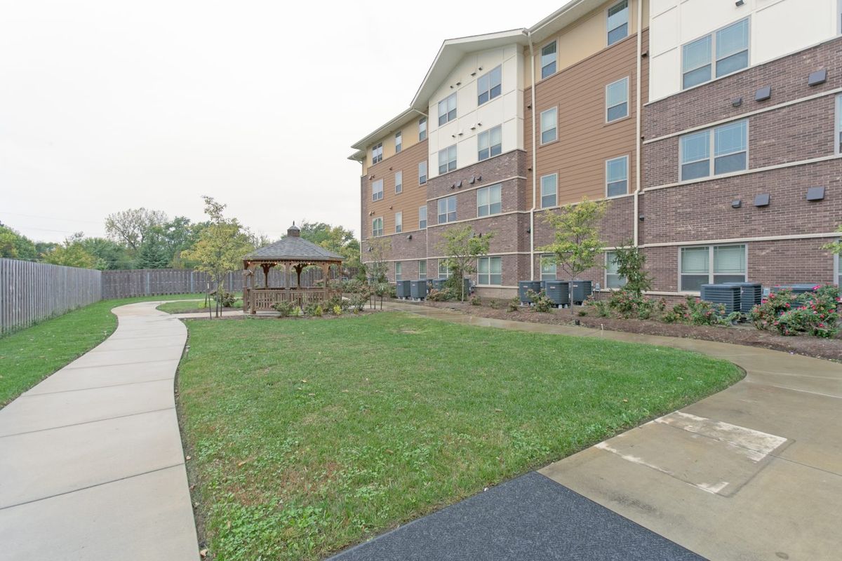 A brick apartment building with a landscaped yard, featuring a gazebo and pathway.