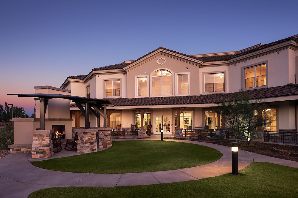 A well-lit residential building with a landscaped lawn at dusk.