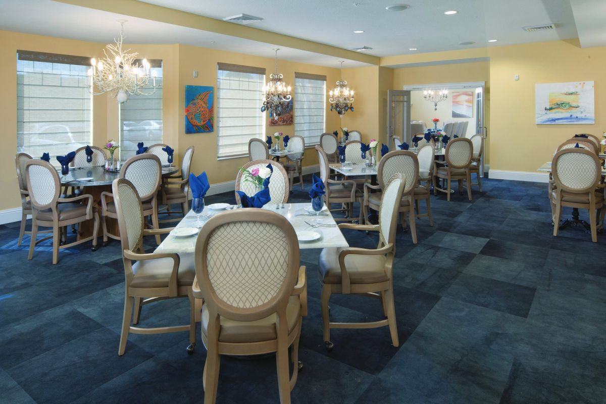 An elegant dining area with neatly arranged tables and chairs, adorned with blue accents and lit by chandeliers.