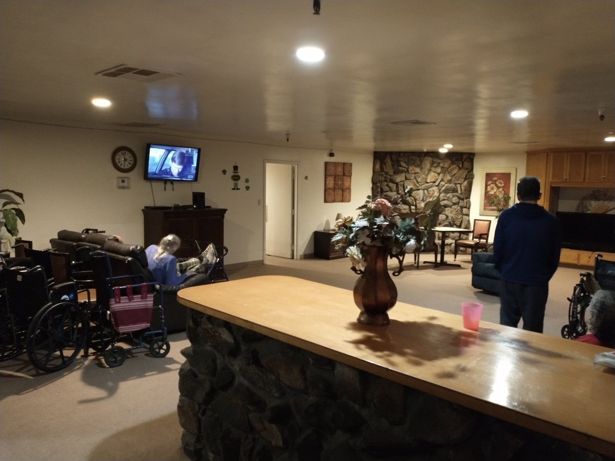 A cozy living room with a television and people relaxing, including one person in a wheelchair.