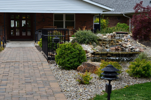 A serene pathway leading to a charming home, featuring a tranquil water feature and lush greenery.