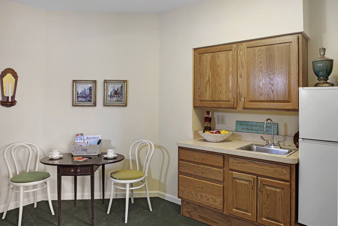 A small kitchen area with wooden cabinets, a sink, and a table with two chairs.