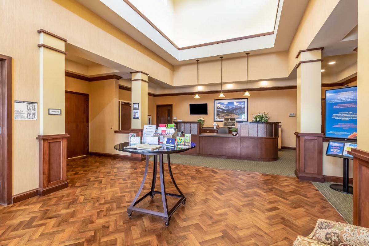 A spacious hotel lobby with a central reception desk and wooden flooring.