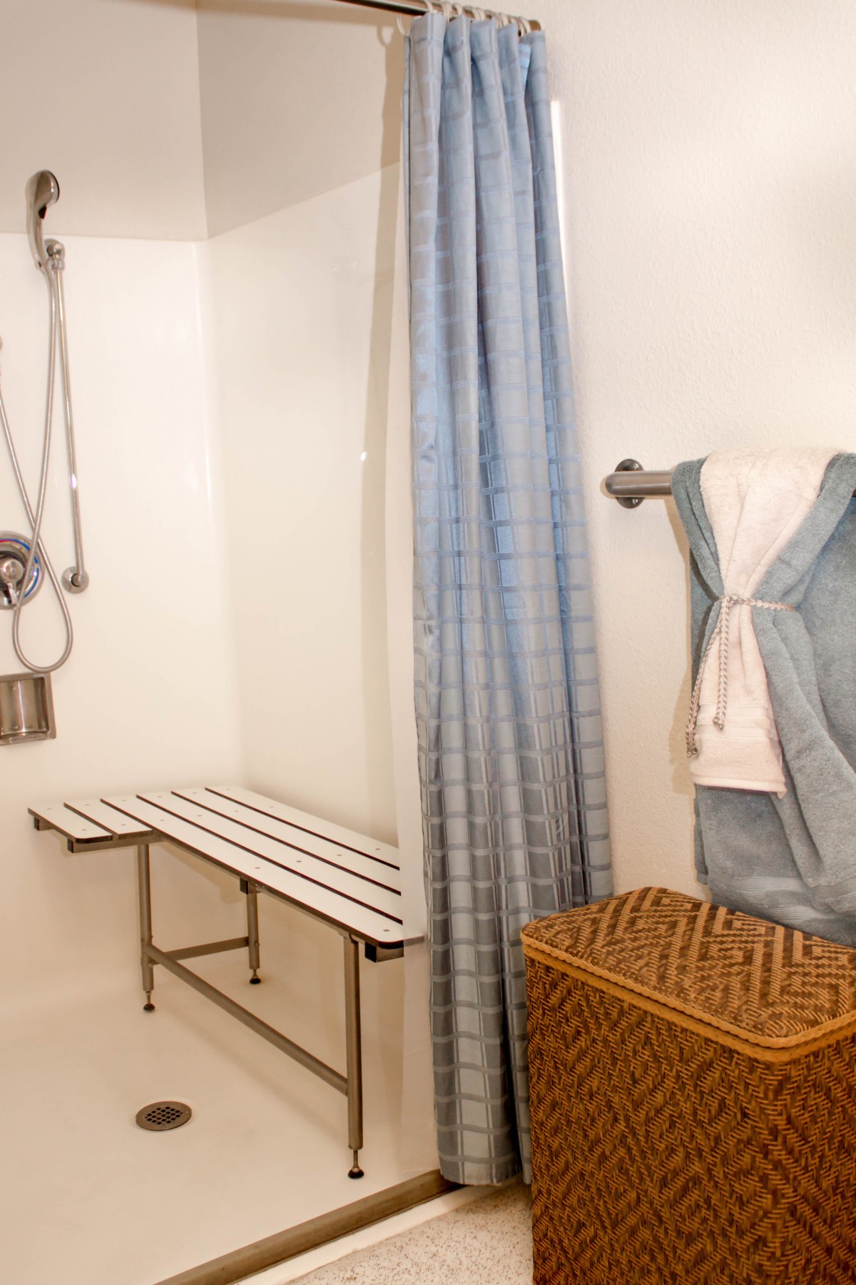 An accessible bathroom with a shower bench and blue curtain.