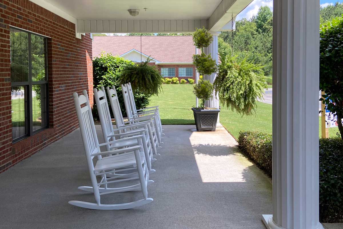 A peaceful porch with white rocking chairs and lush green plants.
