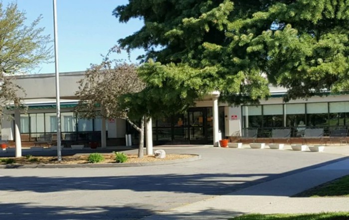The image shows a building entrance surrounded by trees on a sunny day.
