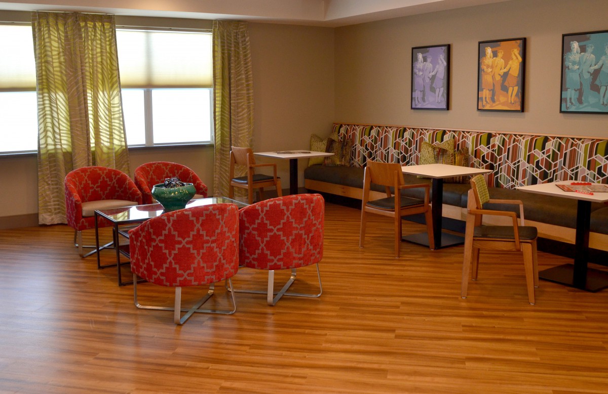 A cozy seating area with red chairs and wooden flooring, featuring tables and wall decorations.