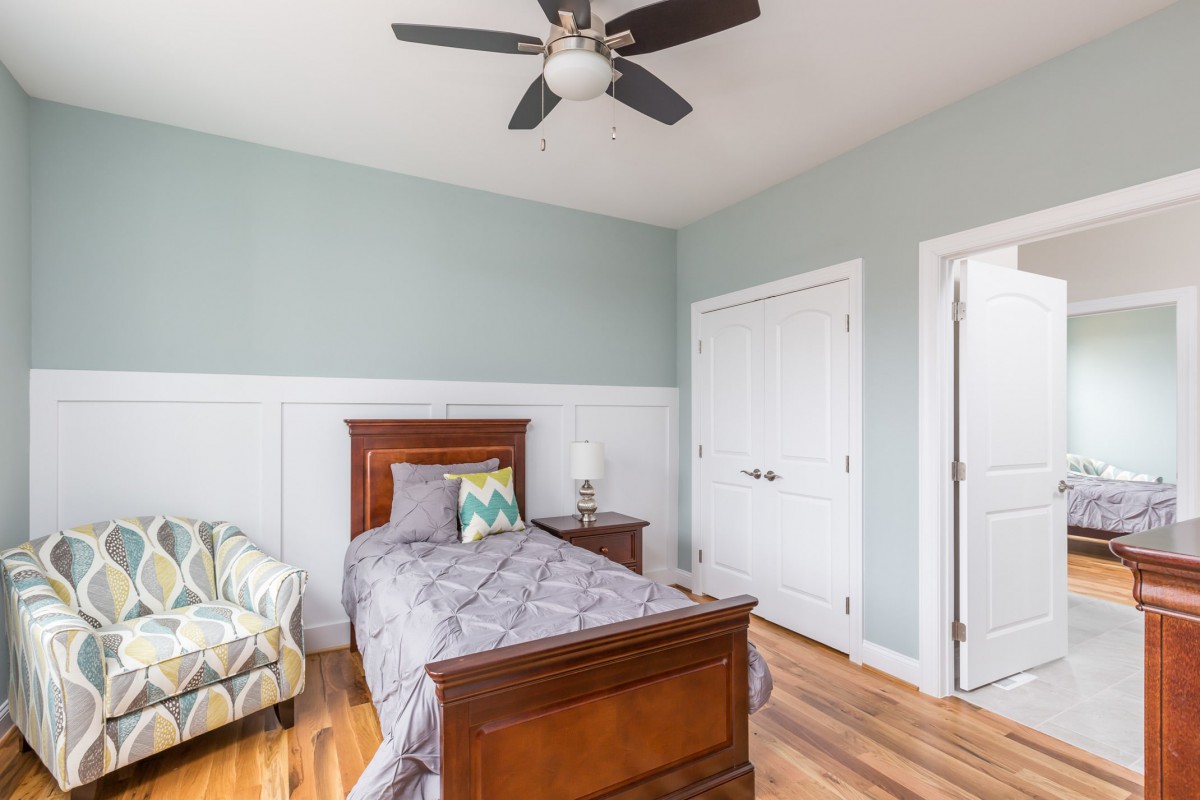 A cozy bedroom with a single wooden bed, ceiling fan, and hardwood floors.