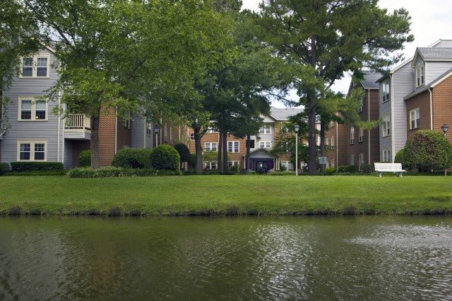 A tranquil scene featuring a pond surrounded by lush greenery and buildings in the background.