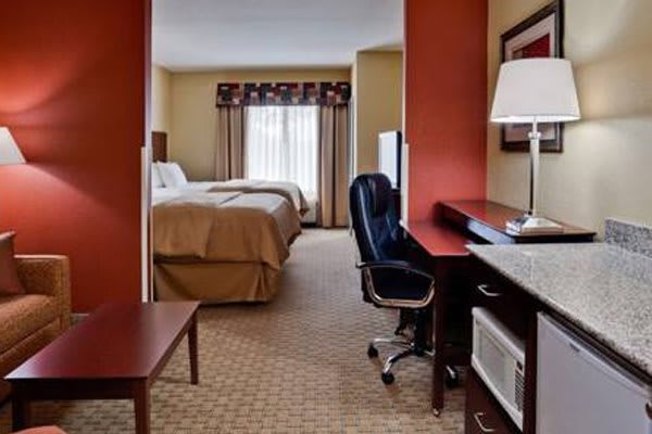 A well-furnished hotel room featuring a bed, desk, chair, and television.
