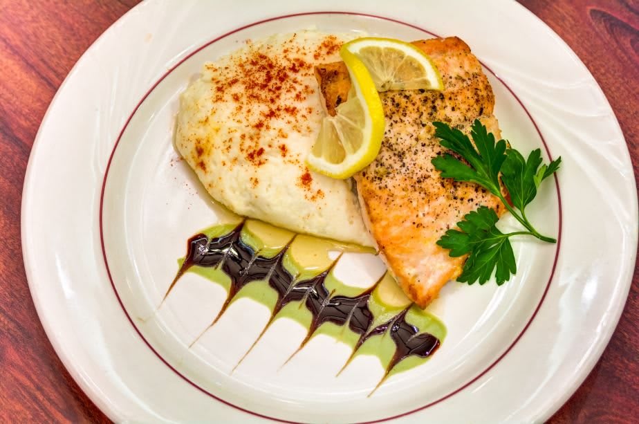 A gourmet dish featuring grilled salmon with a lemon garnish, served alongside creamy mashed potatoes and artistically drizzled balsamic glaze.