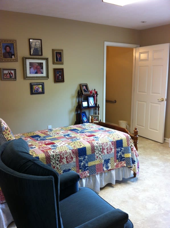 A cozy bedroom with a colorful quilt on the bed, armchair, and photographs on the wall.
