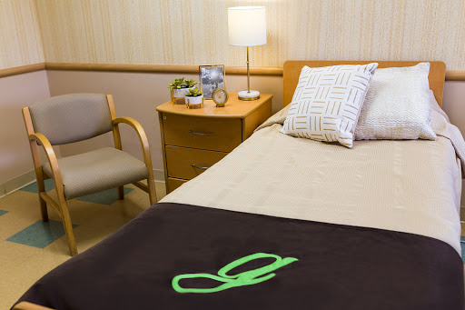 A cozy hospital room featuring a neatly made bed, a comfortable chair, and a table with personal items.