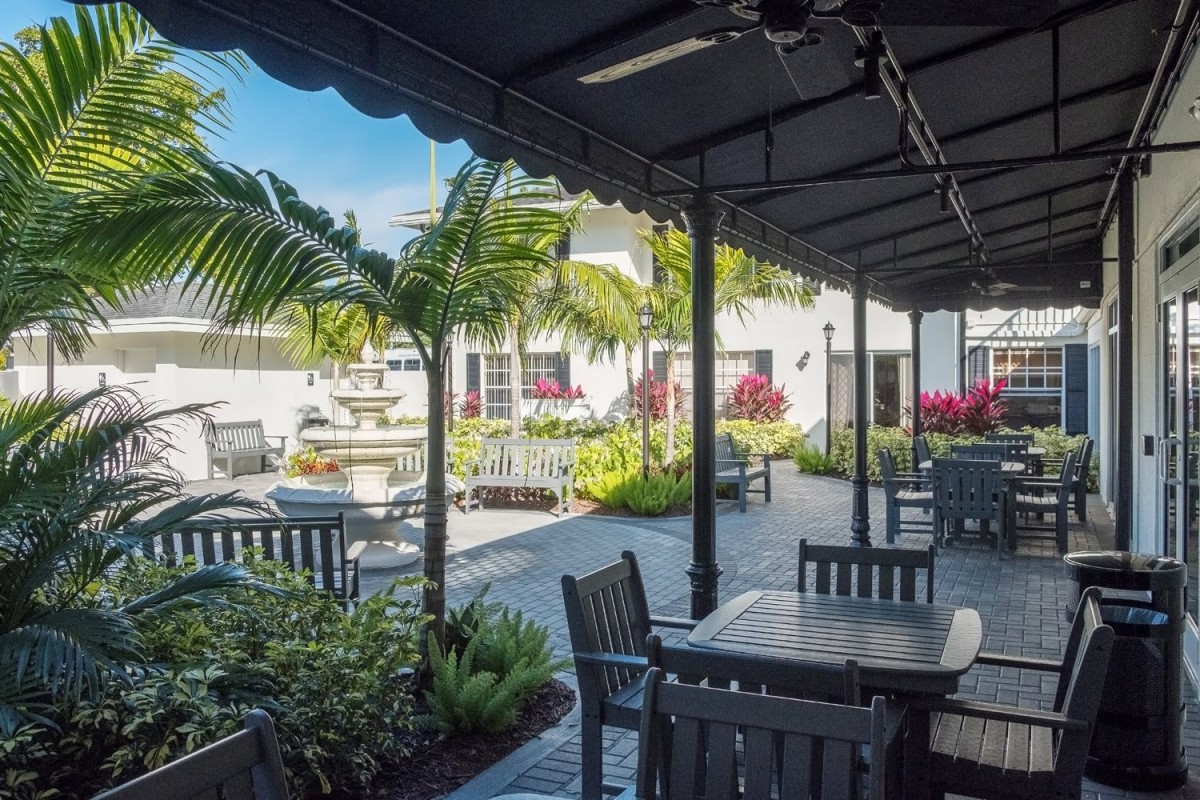 A sunny outdoor patio area with tables, chairs, and lush greenery.