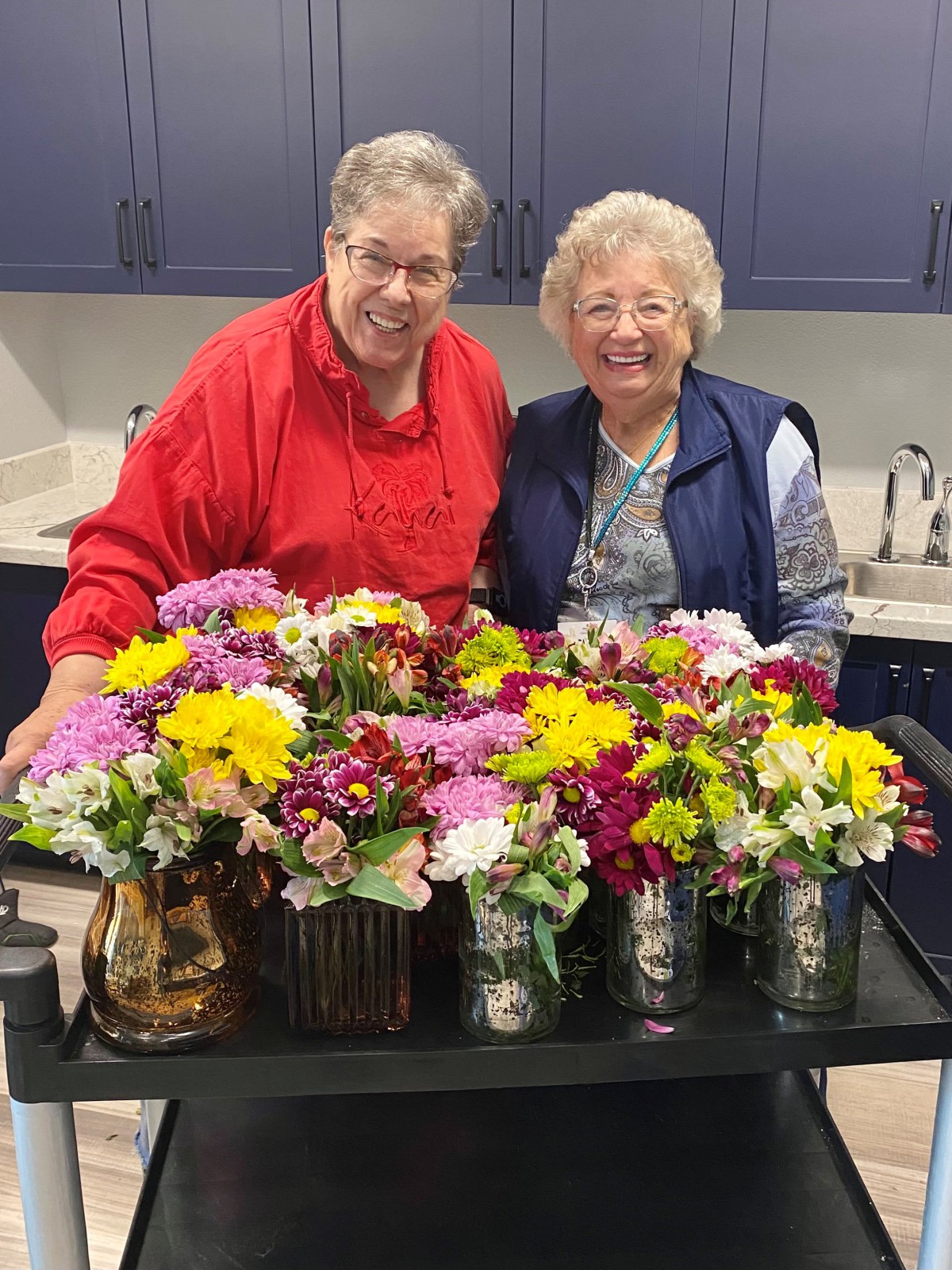 Two people smiling behind a table full of colorful flower arrangements.