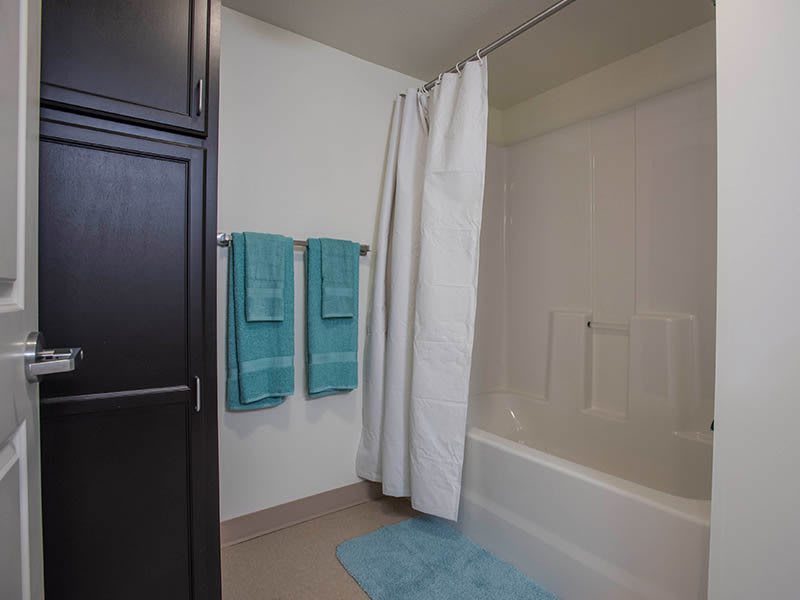A clean and organized bathroom with a shower, bathtub, blue towels, and a matching floor mat.