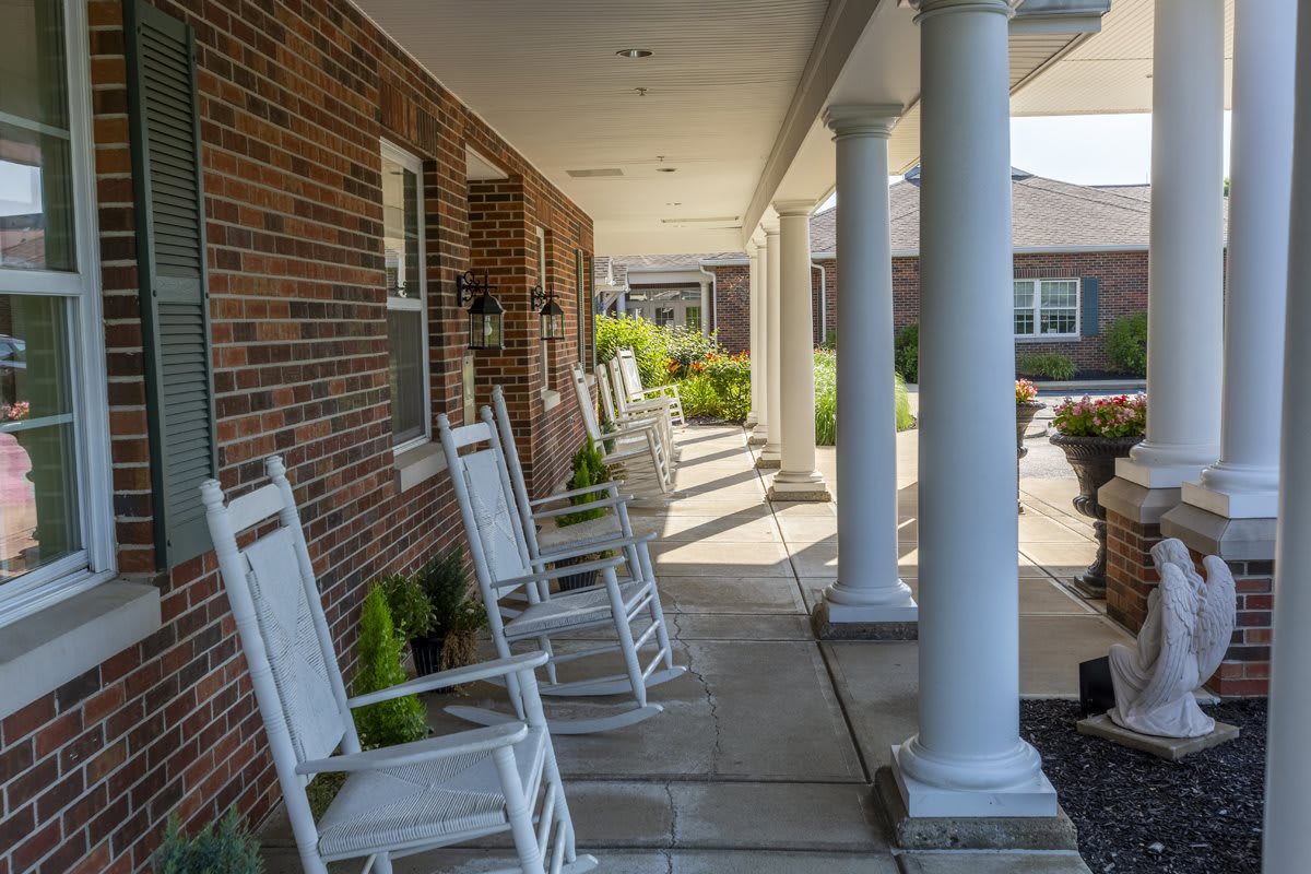A row of white rocking chairs on a shaded porch with brick walls and columns.