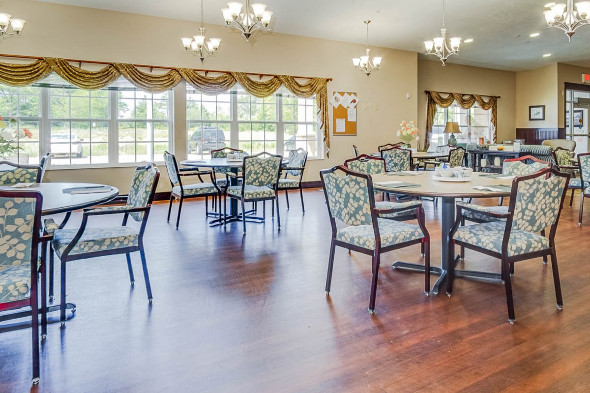 A spacious dining area with multiple tables and chairs, adorned with chandeliers and large windows with decorated curtains.