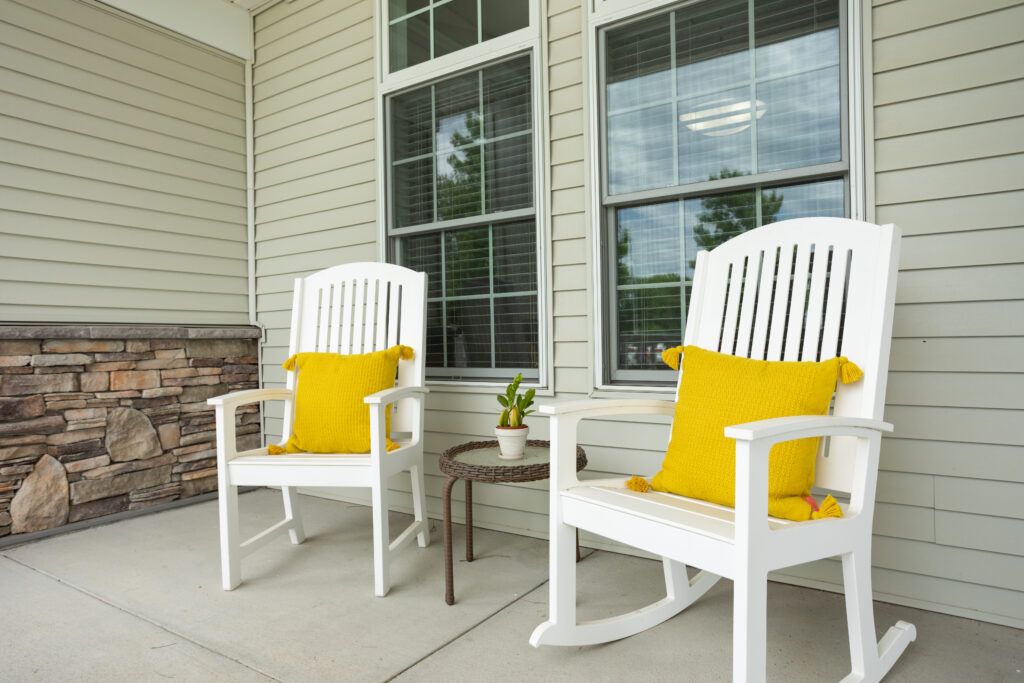 A cozy porch with white rocking chairs and bright yellow pillows beside a small side table.