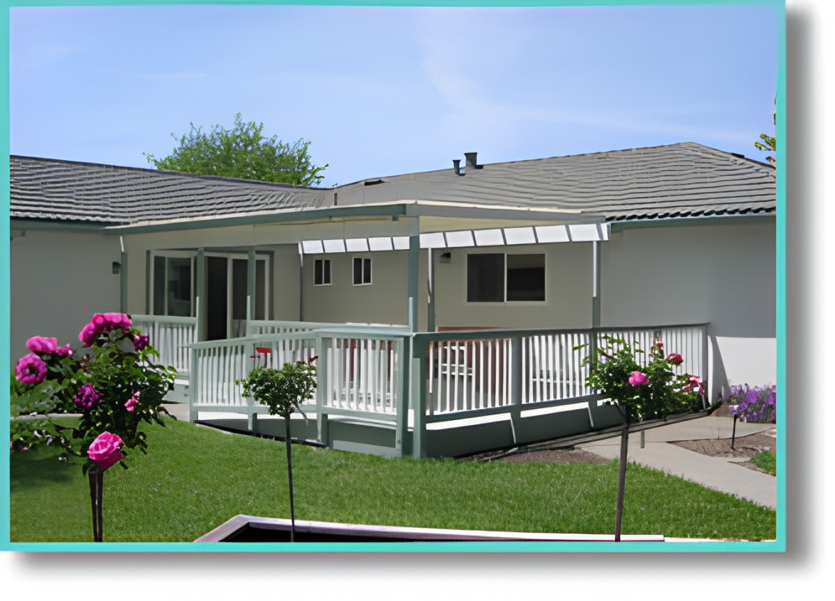 A backyard view of a house with a deck and covered patio, surrounded by a well-maintained lawn and garden.