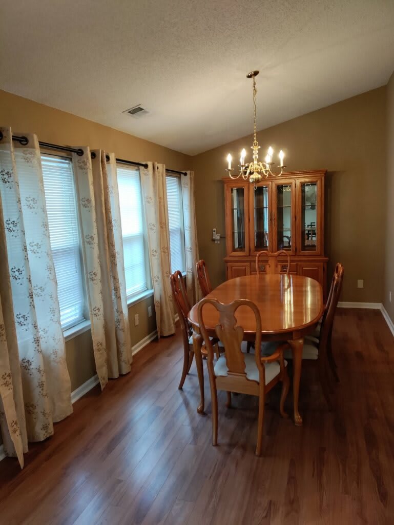 A spacious dining room with a wooden table, matching chairs, and a chandelier overhead.