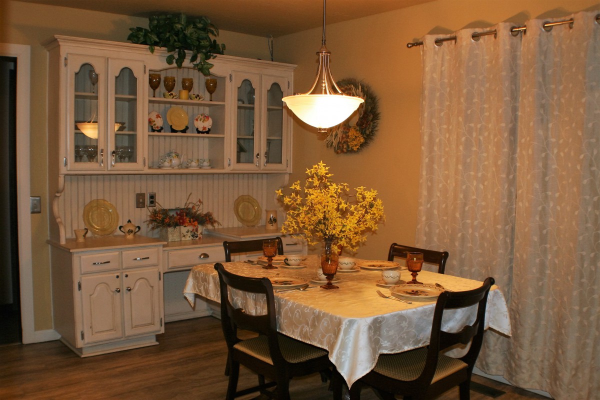 A cozy dining room with a table set for four, featuring decorative flowers and a warm ambiance.