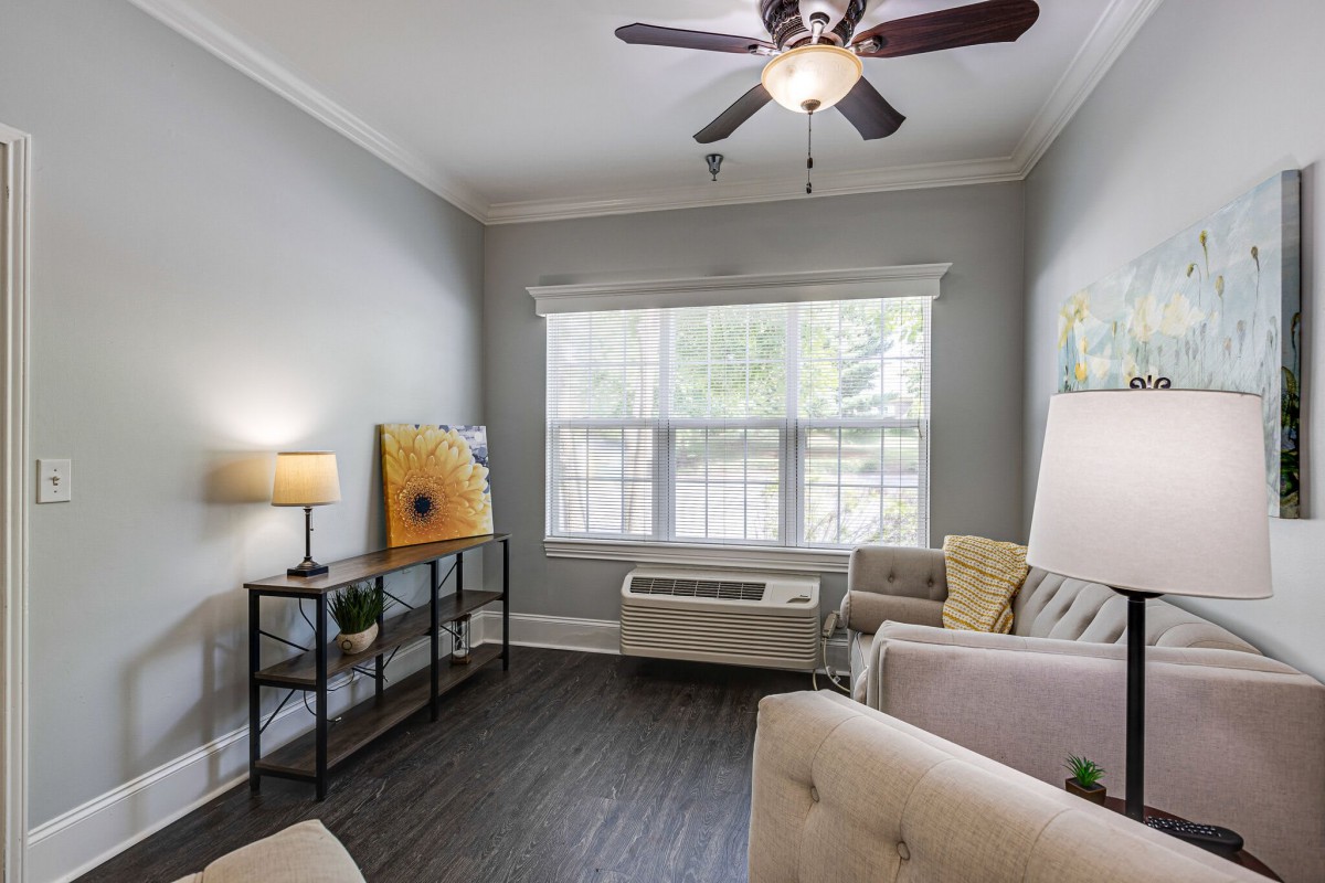 A cozy living room with a sofa, ceiling fan, and large window allowing natural light.