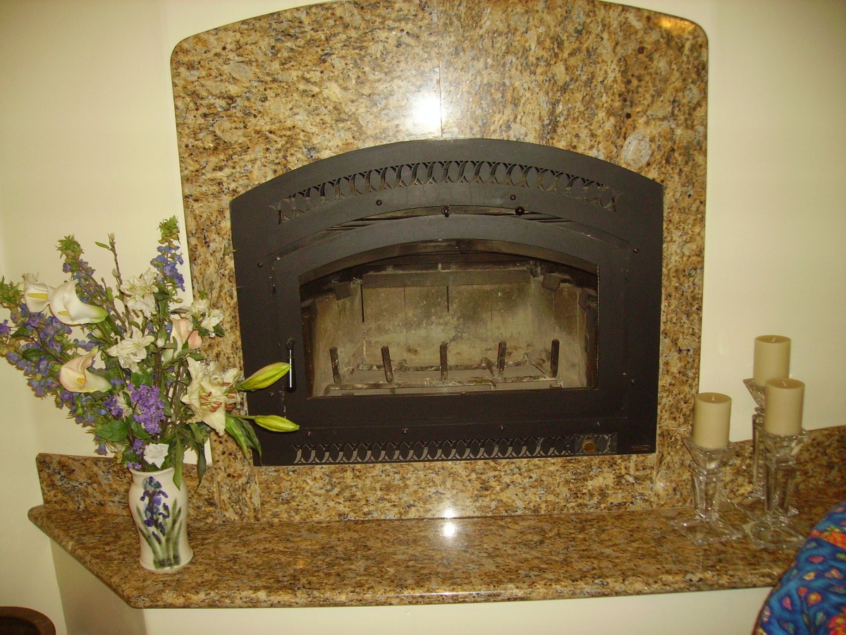 A decorated granite fireplace with a vase of flowers on the side.