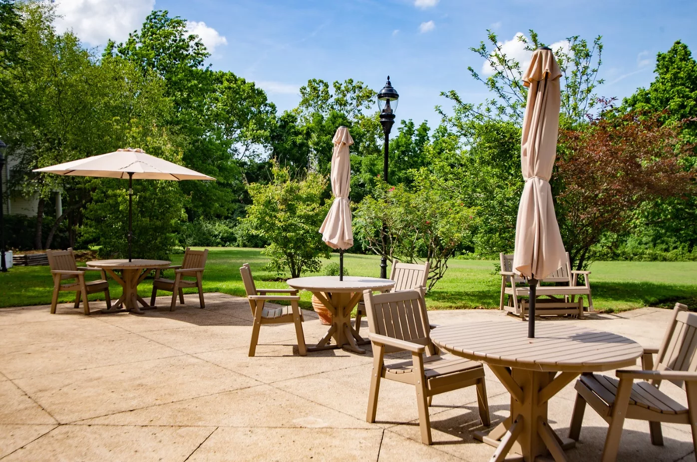 A sunny outdoor patio area with tables, chairs, and umbrellas overlooking a lush garden.