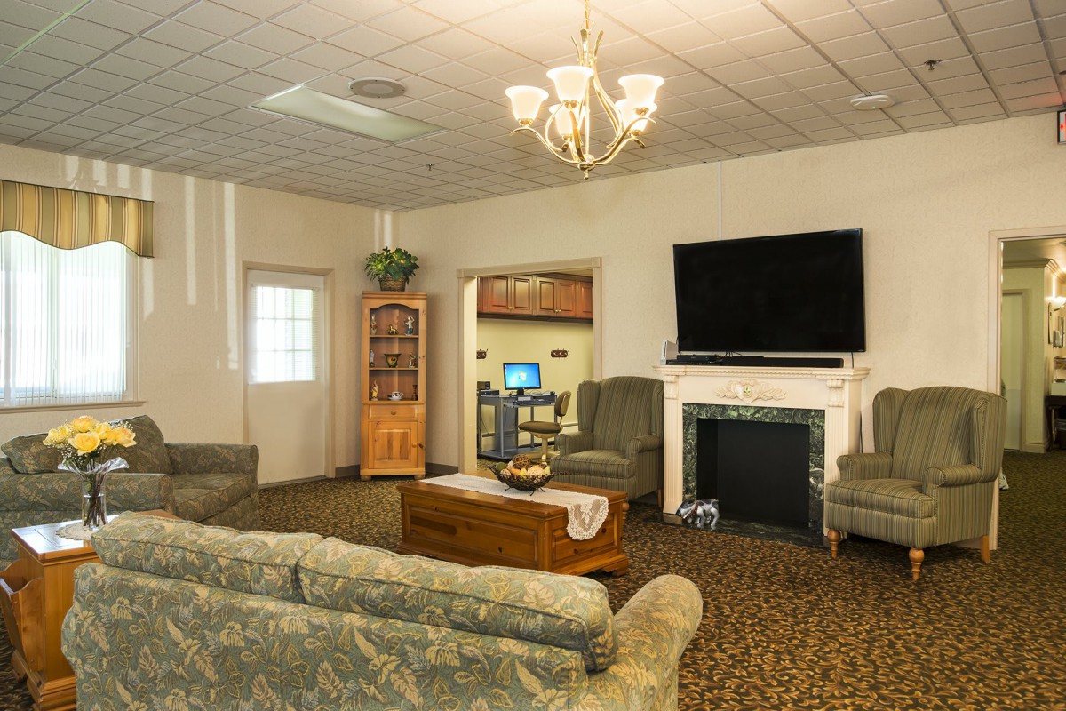 A cozy living room featuring a chandelier, large flat-screen television, fireplace, and comfortable seating arrangements.