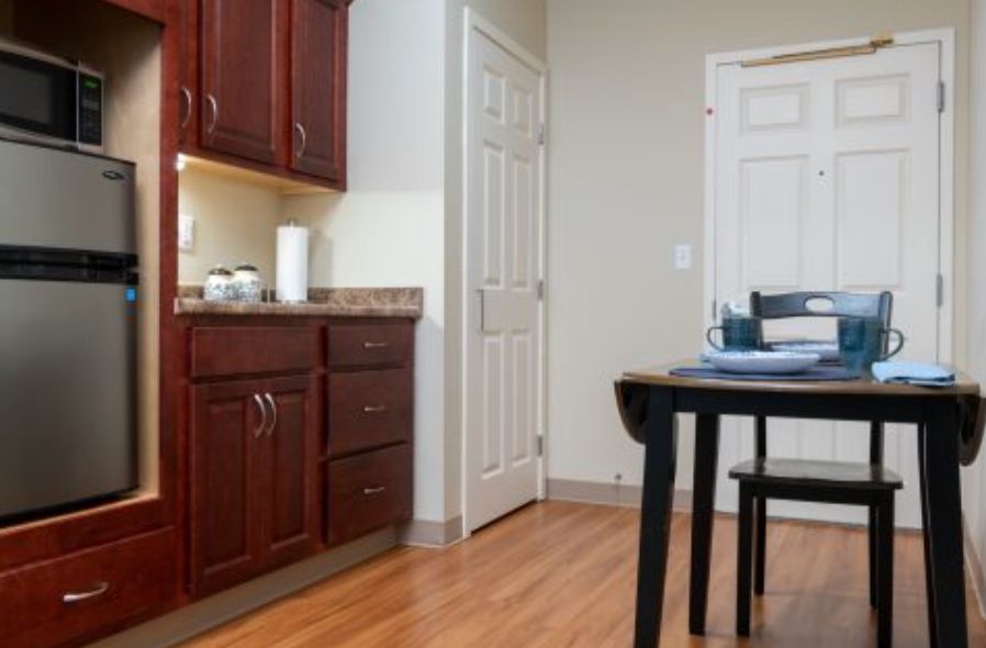A cozy kitchen with wooden cabinets and flooring, featuring a table and white door.