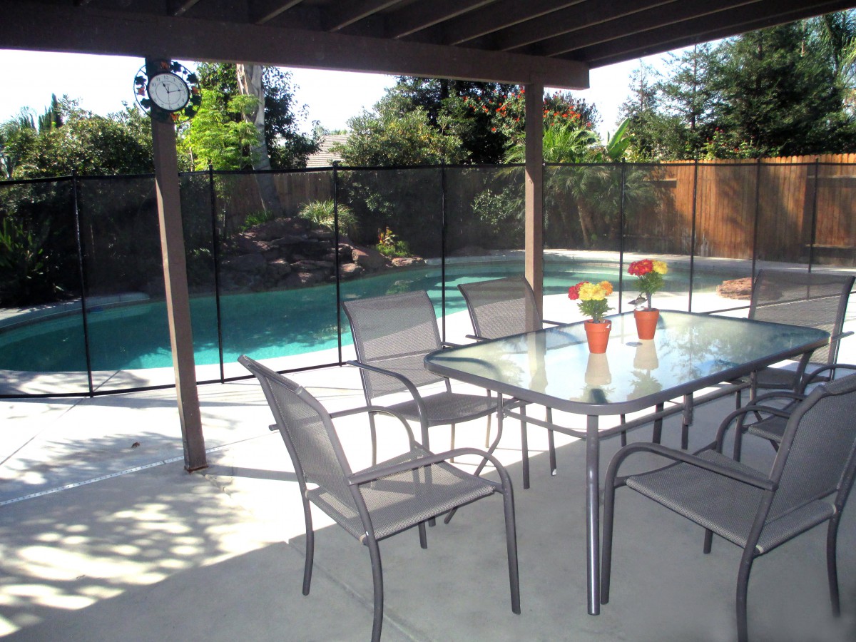 A backyard patio with outdoor furniture overlooking a swimming pool with a safety fence.